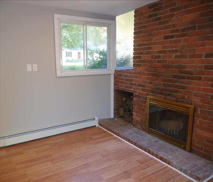 A fireplace in a living room on the basement floor with a window at ground level replaced along with new floors and walls.